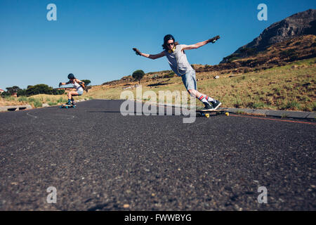 Jeune homme et femme de la planche à roulettes sur la route rurale. Young couple patinage sur la route. Banque D'Images