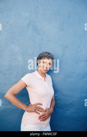 Portrait of young woman posing à huis clos contre fond bleu. Portrait femme debout avec ses mains sur les hanches d'une Banque D'Images