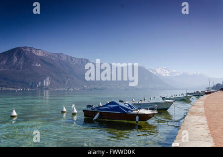 Rangées de bateaux le long de la rive du lac d'annecy avec les montagnes derrière Banque D'Images