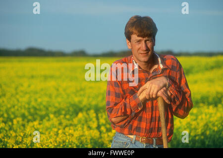 Farmer standing dans un champ de colza en fleurs Banque D'Images