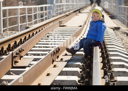 Portrait d'un petit garçon assis sur les rails dans la journée. Bélarus Banque D'Images