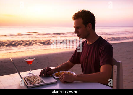 Homme avec portable dans le restaurant de la plage au coucher du soleil Banque D'Images