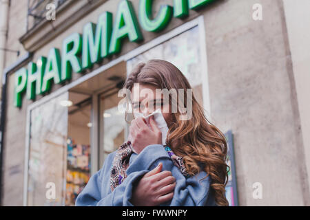 Malade femme froide à côté d'une pharmacie, acheter des médicaments, concept de la grippe Banque D'Images