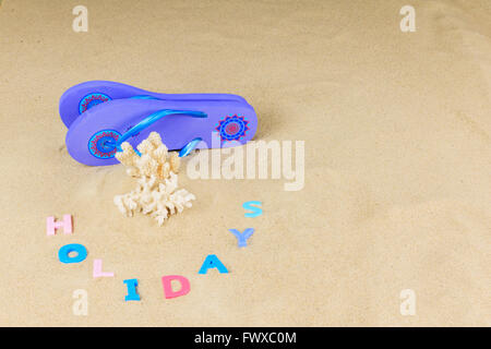 Paire de tongs bleu avec des morceaux de corail et de l'orthographe lettres colorées sur un fond de sable vacances Banque D'Images