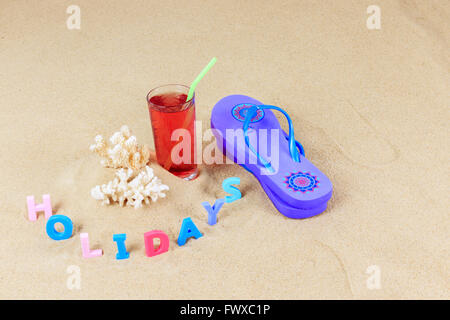 Paire de tongs bleu avec des morceaux de corail, boisson aux fruits en verre avec paille et lettres de couleur sur un sable vacances orthographe Banque D'Images