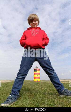 Jeune garçon debout chevauchent en tailleur en face de Pilsum Phare, en Frise orientale, Basse-Saxe, Allemagne Banque D'Images