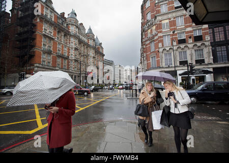 Les jeunes femmes sur un voyage de shopping à Knightsbridge mise à l'abri de la pluie sous les parapluies alors qu'ils traversent la rue, Londres, UK Banque D'Images