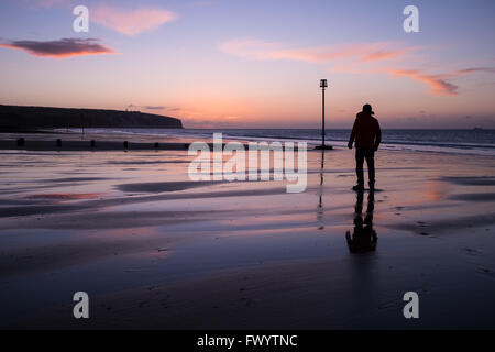 Un homme regardant le lever du soleil sur la plage de Sandown Banque D'Images