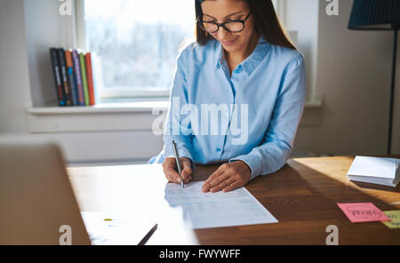 La femme entrepreneur ou propriétaire de petite entreprise travaillant à son bureau à la maison au bureau la rédaction de notes ou sining un docum Banque D'Images