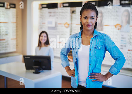 Jeune femme noire smiling standing dans son magasin avec un collègue en backgorund Banque D'Images