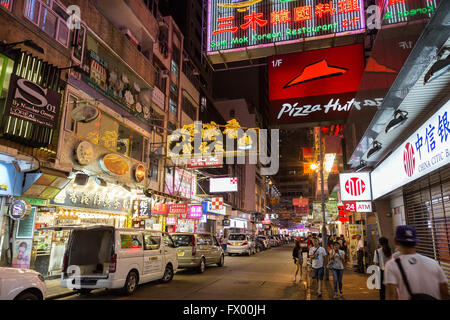 Les gens et les voitures dans une rue pleine de magasins et restaurants de Tsim Sha Tsui, Hong Kong, Chine, la nuit. Banque D'Images