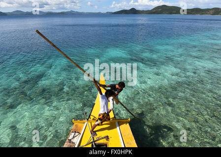 Les garçons d'El Nido, Palawan, Philippines poussant le bateau sur les récifs mis à explorer l'atmosphère reposante et crystal clear bay. Banque D'Images