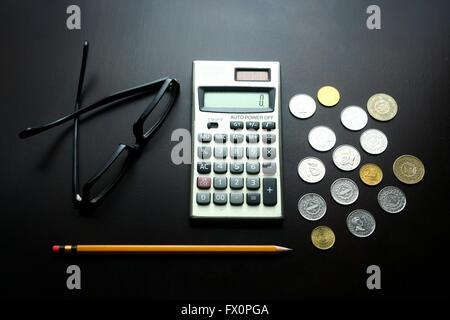 Des lunettes, calculatrice, coins et crayon sur une table en bois Banque D'Images