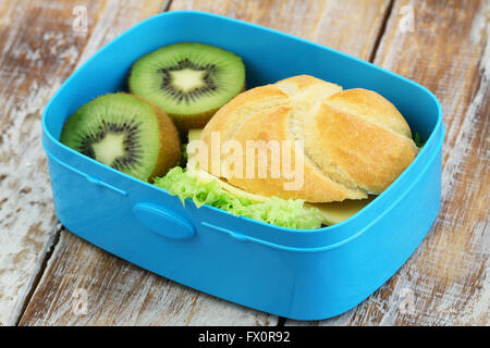 Lunch Box contenant du fromage sandwich et deux moitiés de kiwi sur surface rustique Banque D'Images