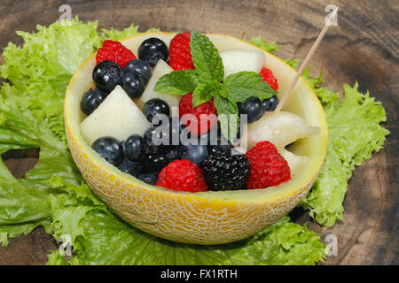 Bits de melons, framboises, mûres et bleuets dans une moitié du melon Galia, évidés et garni de menthe Banque D'Images