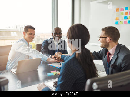 L'équipe entreprise multiraciale réussie travailler ensemble affirment leur engagement en liant les mains autour d'une table de bureau lors d'une m Banque D'Images