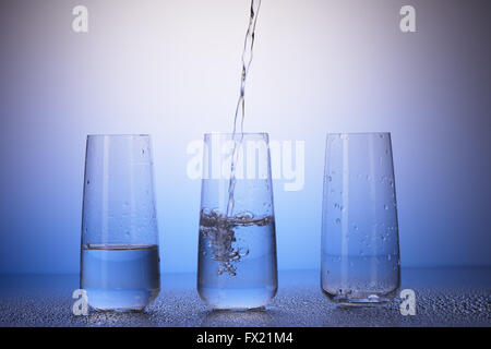 Un tiers pleine, à moitié rempli et vide les verres avec reflet dans les gouttes d'eau sur fond bleu et blanc Banque D'Images