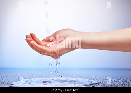 L'eau tombant dans la main de la femme sur fond bleu et blanc Banque D'Images