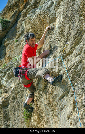 50-60 mature male rock climber en rouge tirant face Banque D'Images