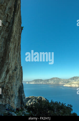 Petit rock climber silhouetté sur falaise abrupte avec la mer bleue derrière Banque D'Images