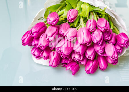 Anniversaire bouquet de fleurs tulipe rose enveloppé dans du papier blanc sur une table en verre Banque D'Images