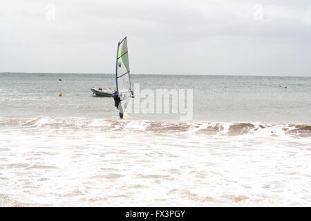 Un homme sur sa planche de surf dans l'eau mousseuse de la planche à voile, planche à voile à la plage de Costa Teguise, Lanzarote, Espagne, concept surf vagues écumeuses Banque D'Images