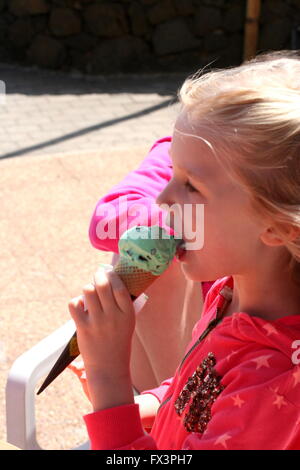 Petite fille blonde kid enfant avoir une saine alimentation lécher la crème glacée sur un cône sous le soleil d'été Banque D'Images