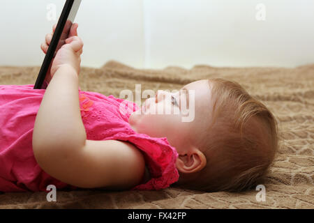 Petite fille mignonne couché sur la table et jouer avec un smartphone Banque D'Images