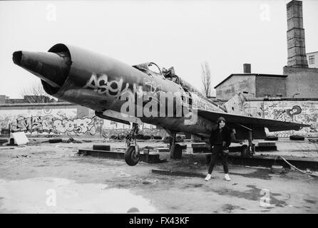 Image d'archive d'une jeune femme en face de chasseurs Mig-21 soviétique, Mutoid Waste company art installation par Kolja Kugler, et des graffitis sur les vestiges du Mur de Berlin, la Potsdamer Platz, Berlin, Allemagne, mars 1994. Autorisation modèle disponible. Banque D'Images