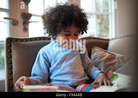 Young Boy Reading Book on Sofa At Home Banque D'Images