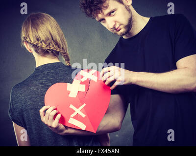 Cœur brisé l'amour difficile concept. Triste Malheureux couple woman and man holding paper cœur rouge fixe avec bandage en plâtre. Dans les relations du Rift. Banque D'Images
