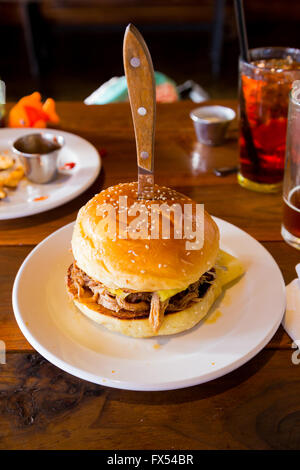 Ce sandwich ou un hamburger sur un petit pain sésame a un couteau dans le dessus de lui et a tiré le porc et les épices et la sauce cubaine sur elle. Banque D'Images