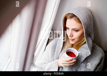 Femme sur appui de fenêtre tenant une tasse de thé Banque D'Images