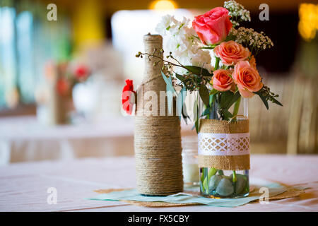 Bricolage Décoration mariage centres de table avec des bouteilles de vin enveloppé dans de la toile de jute et de ficelle rose flowers. Banque D'Images