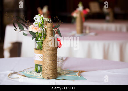 Bricolage Décoration mariage centres de table avec des bouteilles de vin enveloppé dans de la toile de jute et de ficelle rose flowers. Banque D'Images