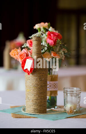 Bricolage Décoration mariage centres de table avec des bouteilles de vin enveloppé dans de la toile de jute et de ficelle rose flowers. Banque D'Images
