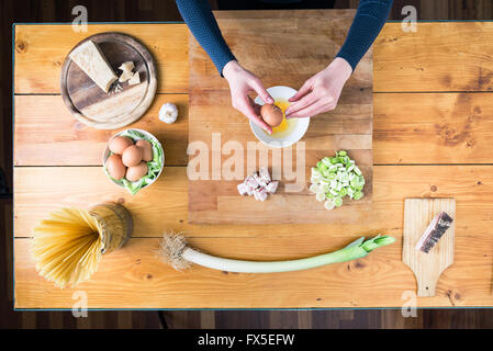 La préparation des pâtes carbonara's. Casser un oeuf les mains des femmes. Banque D'Images