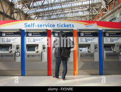 Un homme achète un billet de train à partir d'un self service ticket machine dans une gare Banque D'Images