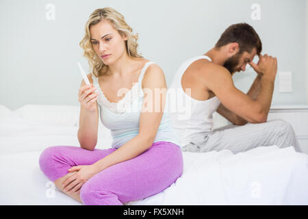 Worried woman looking at test de grossesse on bed Banque D'Images