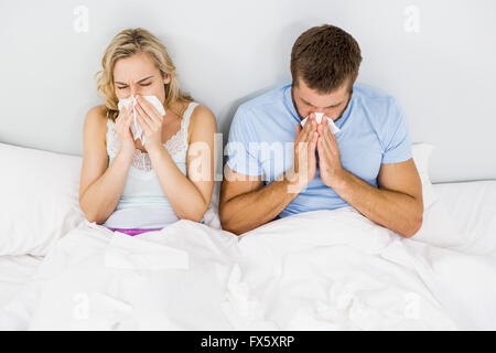 Couple couvrant nez pendant l'éternuement on bed Banque D'Images