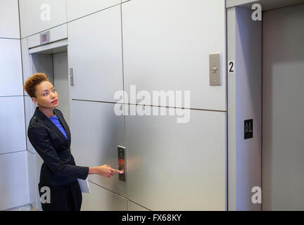 Mixed Race businesswoman en appuyant sur bouton d'ascenseur Banque D'Images