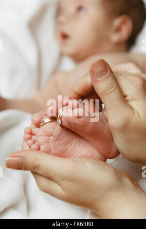 Les pieds de bébé avec les anneaux de mariage dans les mains de la mère Banque D'Images