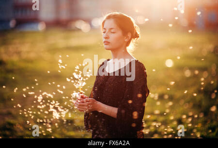 Caucasian woman standing in field with blowing dandelion seeds Banque D'Images