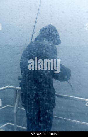 Caucasian fisherman standing on rainy pont de bateau Banque D'Images