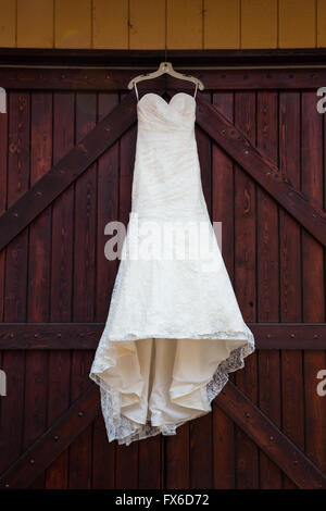 Robe de mariée blanche accroché sur les grandes portes colorées marron dans un vignoble dans l'Oregon. Banque D'Images