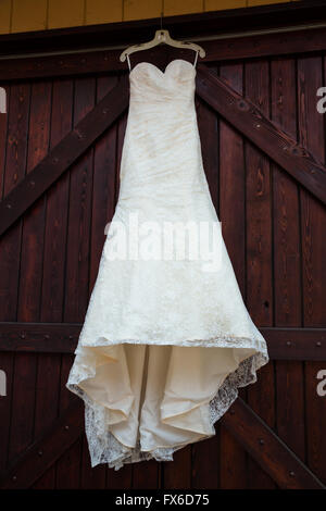 Robe de mariée blanche accroché sur les grandes portes colorées marron dans un vignoble dans l'Oregon. Banque D'Images