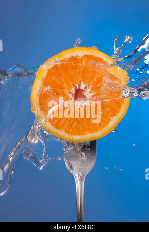 La moitié des fruits orange sur fourche avec de l'eau splash et vide fond bleu. Concept Santé photo, idéal pour poster ou campagne. Banque D'Images