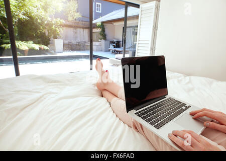 Image Gros plan femme de se détendre dans la chambre et le surf internet sur son portable. Femme assise sur le lit et de travailler sur son ordinateur portable co Banque D'Images