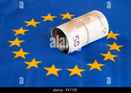Rouleau de bande en caoutchouc avec de l'argent, plusieurs billets de banque, d'Euros sur drapeau européen Banque D'Images