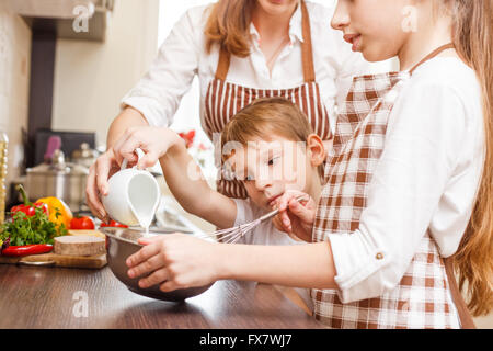 Mère avec des enfants la cuisson des œufs brouillés ou omelette dans la cuisine. Arrière-plan de cuisine familiale Banque D'Images